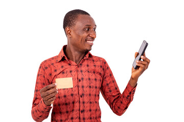 Young man holding a credit card and looking at his mobile phone smiling.