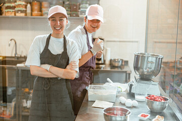 Positive women in aprons smile to camera standing in craft bakery shop