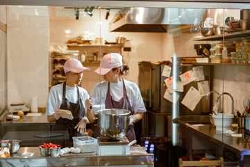 Fototapeta na wymiar Woman shows recipe to colleague making dough at table in bakery