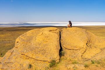 Teen tourist girl sitting on sandstones against beautiful summer landscape of steppe and salt lake....