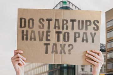 The question " Do startups have to pay tax? " on a banner in men's hand with blurred background. Business. Entrepreneur. Rate. Difficulty. Payment. Innovation. Innovative