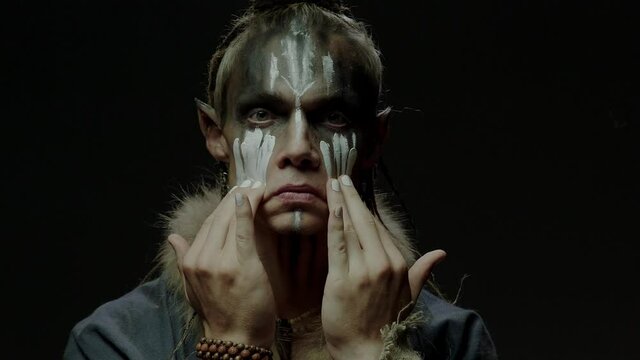 Elf shaman applies white paint to put on ritual makeup