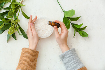 Woman adding essential oil to sea salt on white background, top view