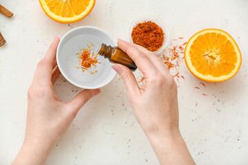 Woman adding essential oil to water in bowl on white background, top view
