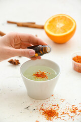 Woman adding essential oil to water in bowl on white background