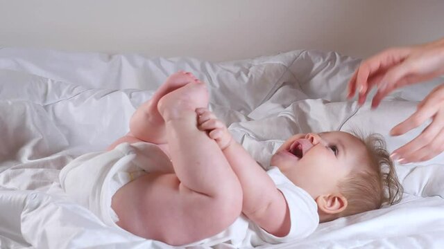 Woman hands tickle adorable 7 month baby girl lying on the bed 
