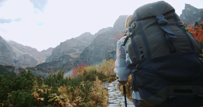 Young man hiker backpacker walking stone trail to mountain peaks overlooking amazing highlands landscape on autumn day. Adventure travel explorer. Fall season trekking in mountains