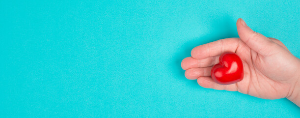 Woman is holding a red heart in her hand, blue colored background, copy space