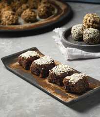 A sweet dessert of dried fruits covered with sesame seeds lies on a ceramic stand, next to a variety of oatmeal balls in a plate. Close-up, healthy eating, trend, selective focus..