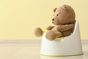 Cute toy bear sitting on potty near color wall