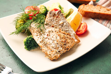 Plate with tasty baked cod fillet and vegetables on color background, closeup