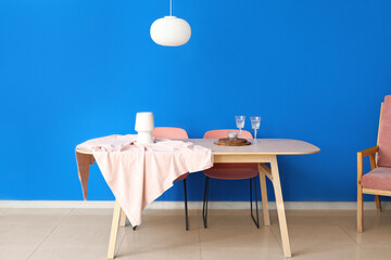 Dining table with lamp and glasses near color wall