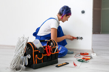Female electrician repairing socket in room