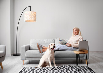 Mature woman with cute Labrador dog reading magazine at home