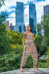 Dressing in a strapless fashionable, contemporary style dress top, pants, a young pretty black woman is standing outside a busy business district, looking forward..