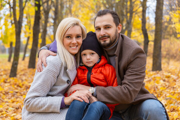 Fototapeta premium Happy family sitting on dry leaves and looking at camera