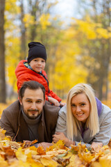 Happy family laying on dry leaves and looking at camera