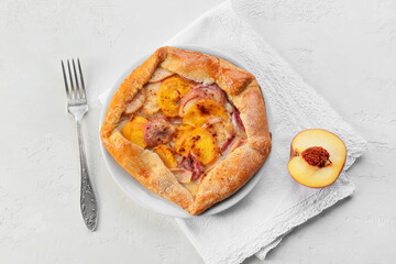 Plate with tasty peach galette on light background