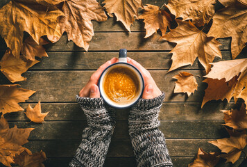 Fototapeta Hands of a caucasian male holding a hot coffee cup on an aged wooden table with autumn leaves around it. Homey feeling and relax. obraz