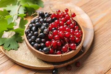 Bowl with ripe red and black currant on wooden background, closeup