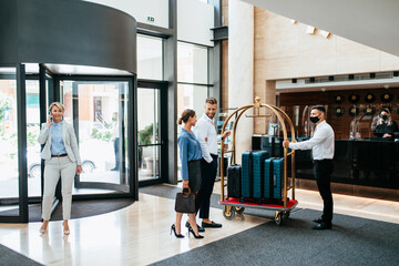 Bellboy helping guests with their luggage cart in hotel hallway. He takes guests' luggage to their rooms. - Powered by Adobe