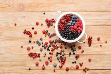 Colander with different ripe berries on wooden background