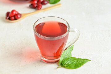 Cup of healthy dogwood berry drink on light background