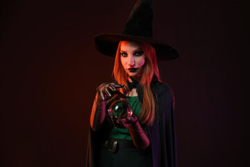 Young witch with crystal ball on dark background