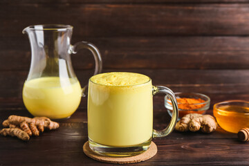 Obraz na płótnie Canvas Glass and jug of healthy turmeric latte on wooden background