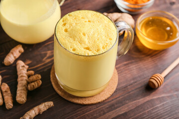 Glass cup of healthy turmeric latte and honey on wooden background, closeup
