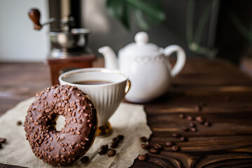 Morning tea with sweet doughnut. A white vintage cup of coffee next to a teapot and freshly ground coffee in an antique coffee grinder