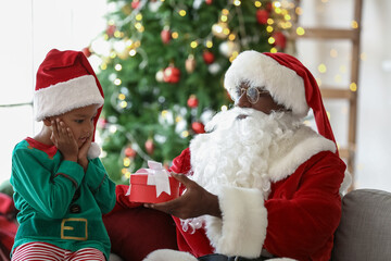 Santa Claus giving present lo little African-American boy at home