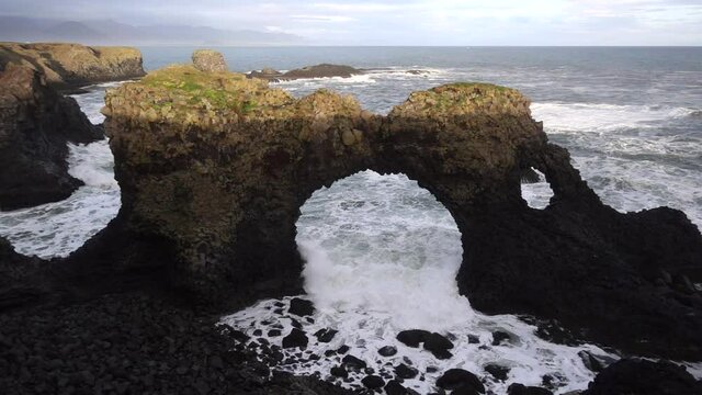 Waves smashing in slow motion through picturesque Gatklettur or Hellnar Arch that is a circular stone arch and rock formations naturally shaped by waves from the North Atlantic. Gatklettur is located 