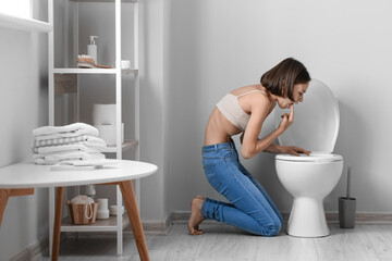 Young woman near toilet bowl in bathroom. Anorexia concept - obrazy, fototapety, plakaty