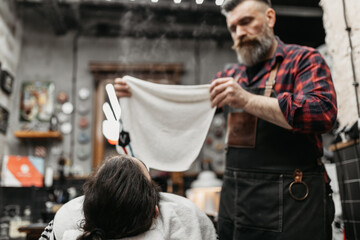 A barber trims a young guy's beard in his barber shop.
