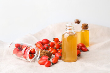 Bottles of essential oil and rose hip berries on light background