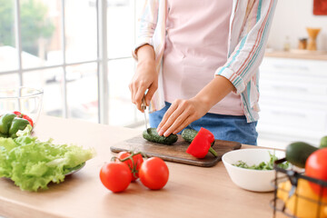Young woman cutting fresh vegetables in kitchen