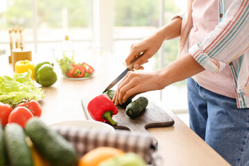 Obraz na płótnie Canvas Young woman cutting fresh vegetables in kitchen