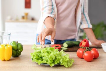 Young woman with fresh vegetables on table in kitchen