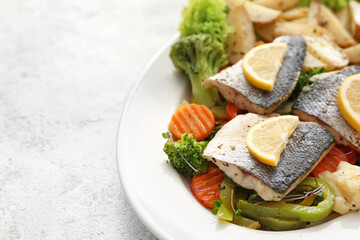 Plate of tasty sea bass fish with vegetables on light background