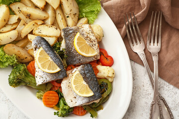 Plate of tasty sea bass fish with vegetables on light background