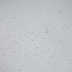 Wet with water drops glass window with light grey rainy background, closeup.
