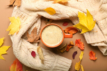 Composition with cup of coffee, sweater and autumn leaves on brown background