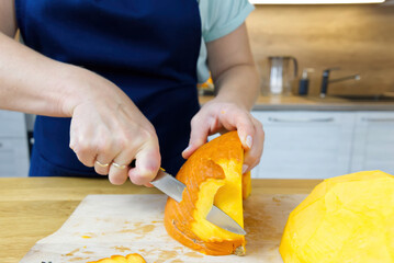 woman hands removs the skin from pumpkin with knife