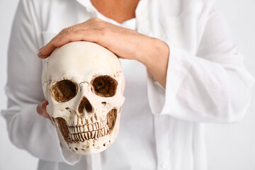 Woman holding human skull on white background