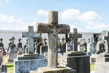 Fototapeta premium Stone cross with Jesus and graves with more crosses in the cemetery blurred behind.