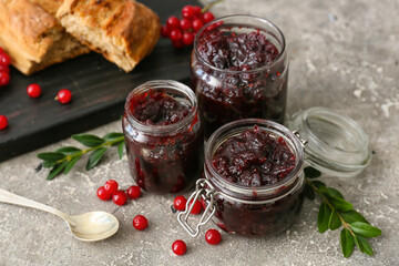 Jars of tasty lingonberry jam on grey background