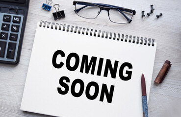 Notepad with the inscription COMING SOON. Conceptual image, business accessories, calculator isolated on the desktop. Finance or business concept.