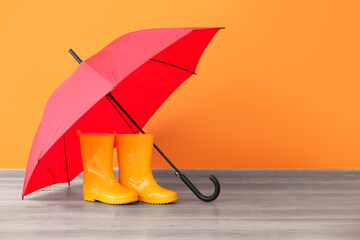 Rubber rain boots with umbrella on floor near color wall