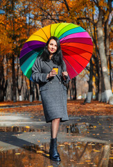 Obraz premium Young happy woman in a coat under an umbrella. Young girl with long black hair with an umbrella in the autumn park. 